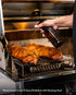 Texas-style pork ribs being spritzed on a roasting rack above a drip pan inside a Tucker R Class BBQ