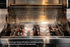 Tucker R Class BBQ with glowing charcoal in the stainless steel charcoal tray beneath the open hood